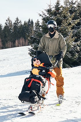 Portrait von einem Biskifahrer und seinem Begleitläufer. Der Begleitläufer trägt eine große, verspiegelte Skibrille.