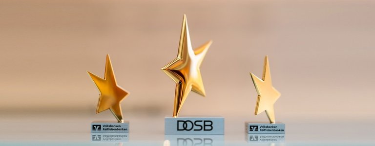 Das Bild zeigt drei Trophäen der Sterne des Sports. Es sind goldene Sterne auf silbernem Sockel.